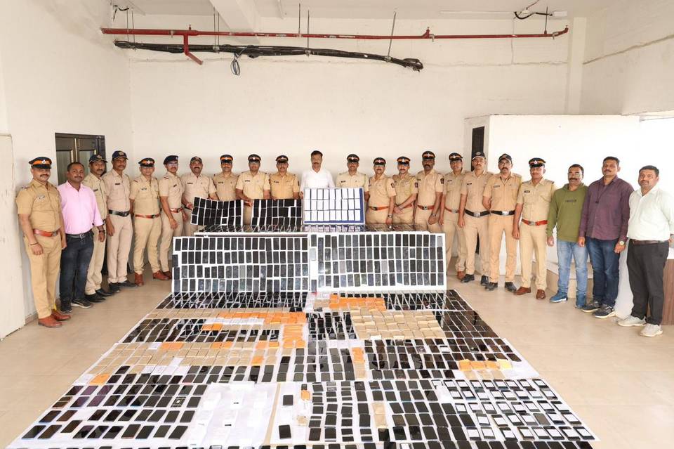 Police officers standing behind hundreds of recovered mobile phones laid out on the floor and on display boards